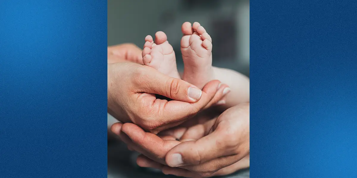 Closeup of new parents’ hands holding their newborn baby.