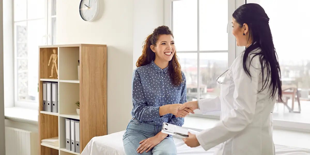 Smiling young woman shaking the hand of a female doctor at an appointment.