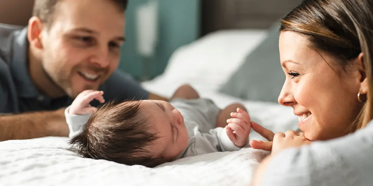 Young couple looking lovingly at their newborn baby on a bed.