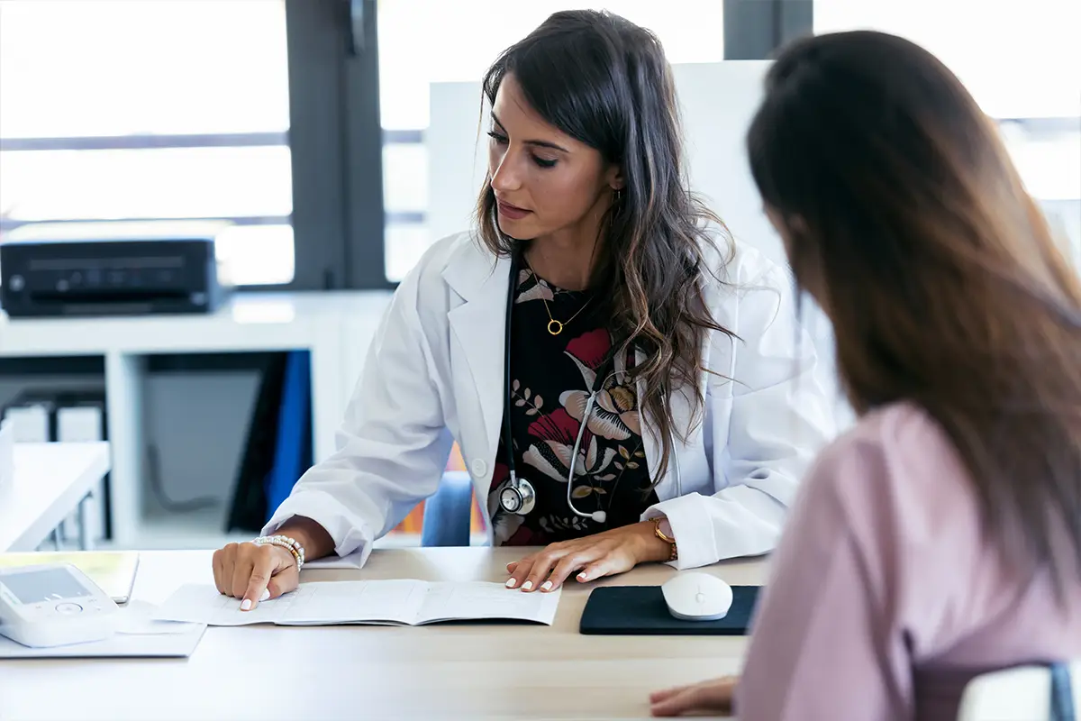 Young hispanic female doctor reviewing medical records with her female patient.