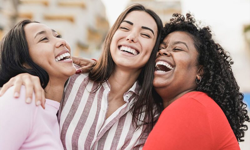 Three female friends, smiling and holding each other.