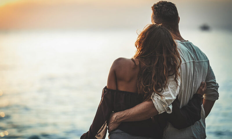 Attractive young couple holding each other in front of the beach.