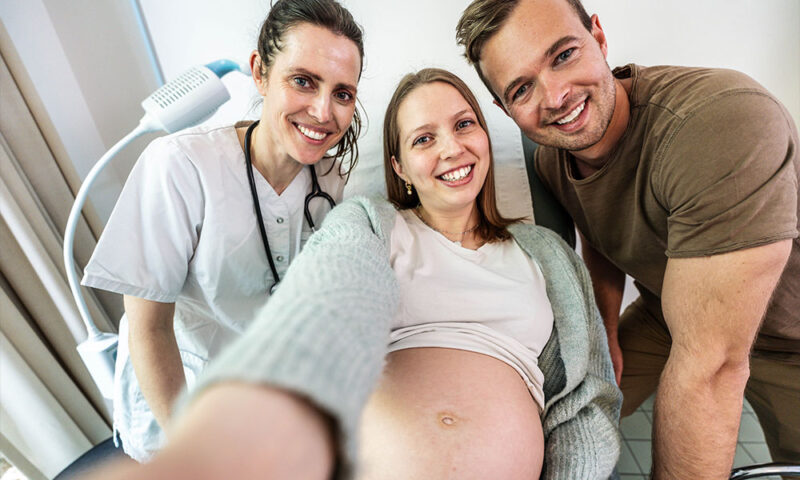 Female doctor posing for a selfie with a pregnant caucasian couple