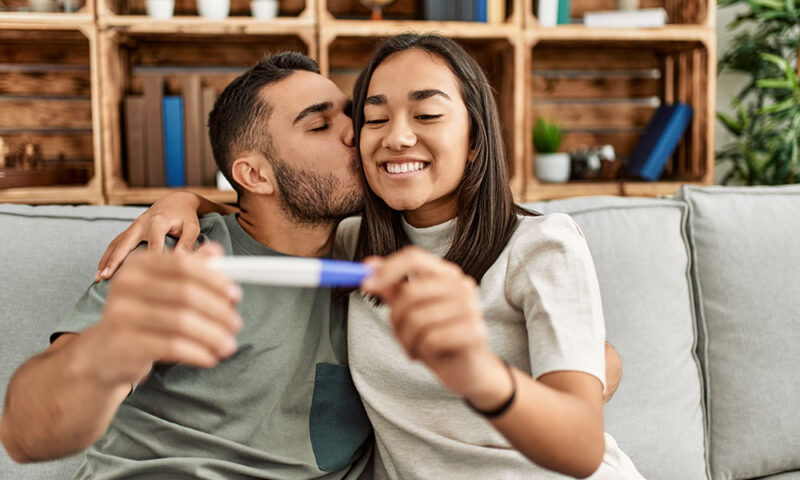 Young, happy ethnically ambiguous couple holding a positive pregnancy test